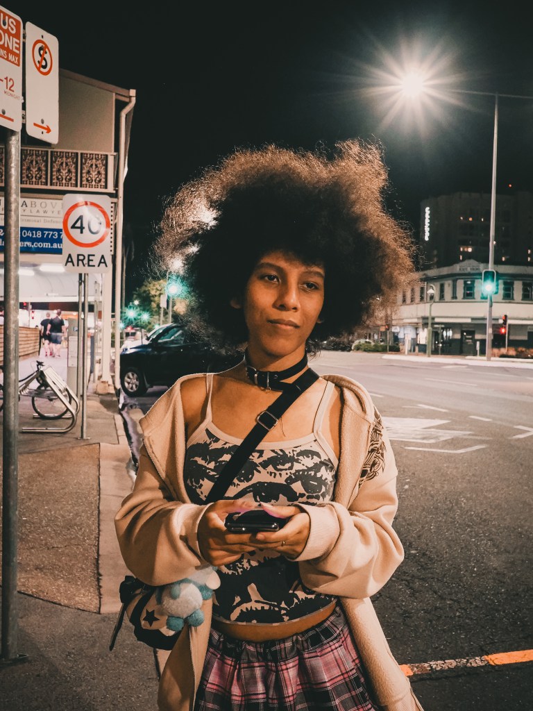 Woman at a bus stop at night holding a camera, street photography portrait.