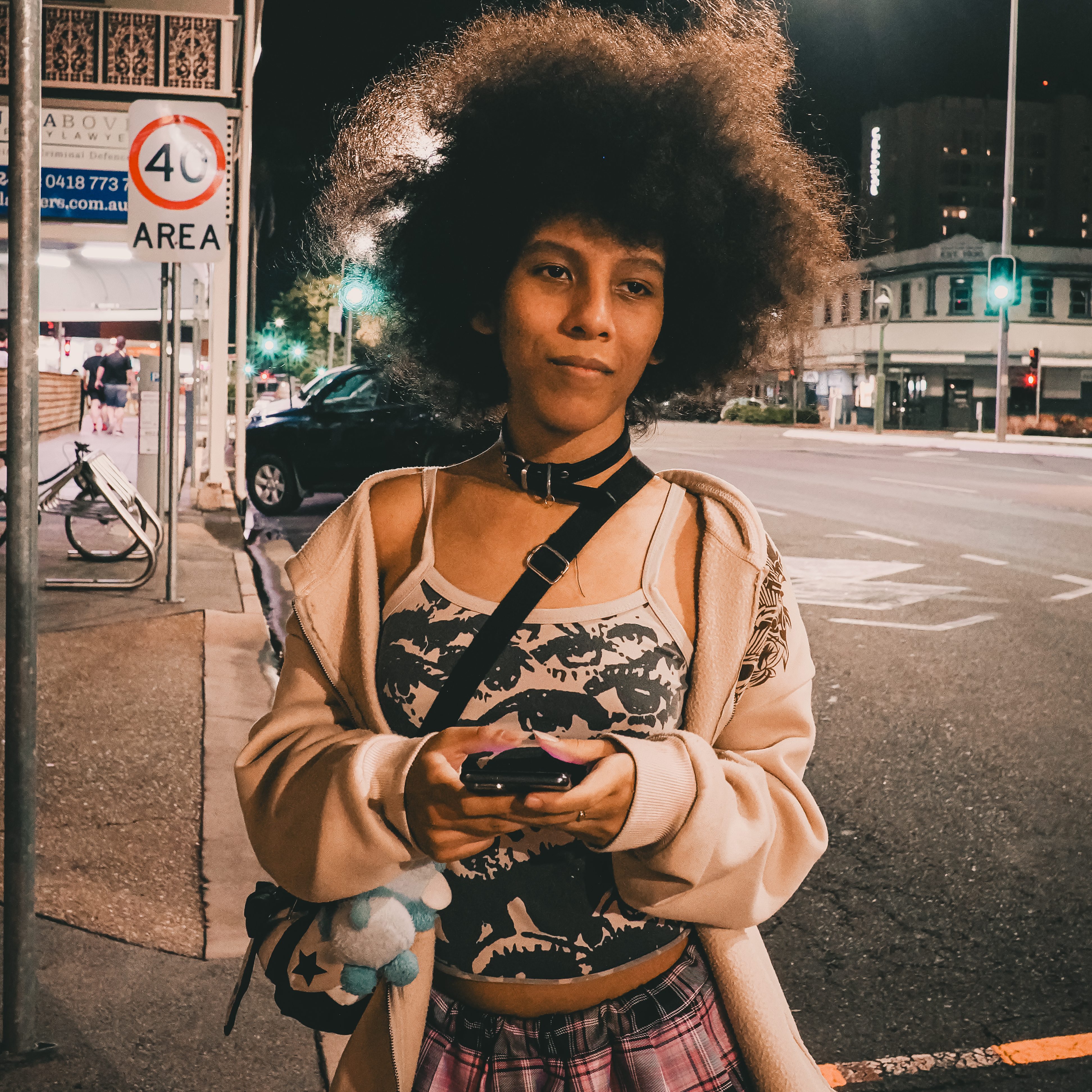 Woman at a bus stop at night holding a camera, street photography portrait.