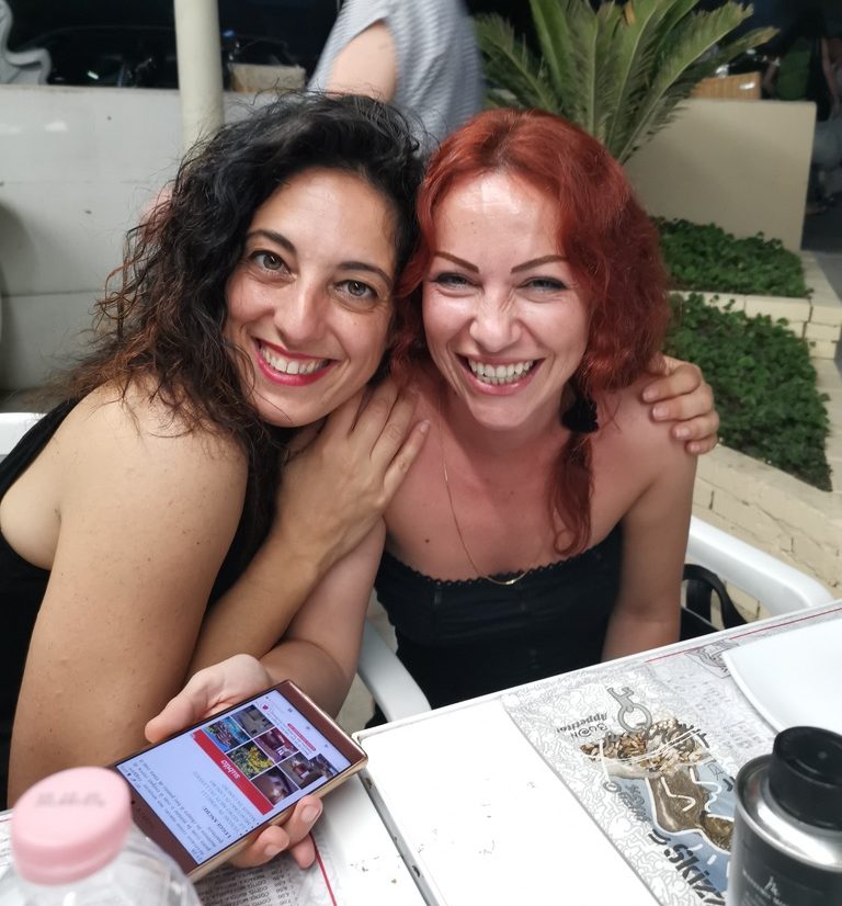 Two women smiling and hugging at a table during a joyful reunion