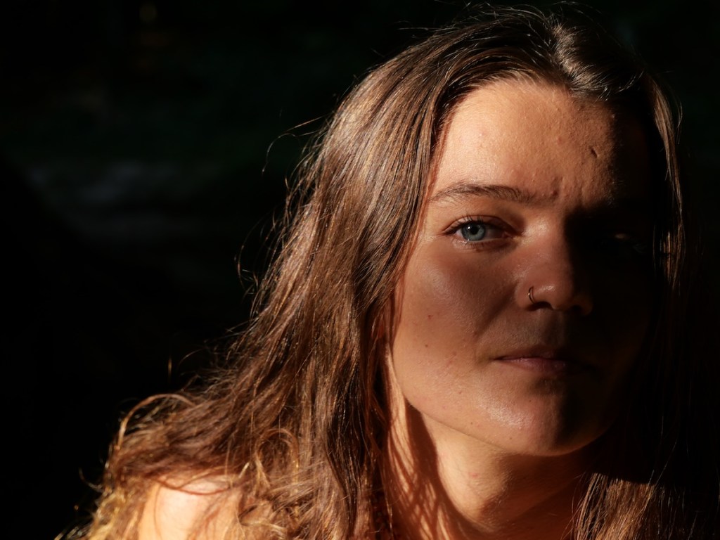 Woman partially lit by natural light, calm expression, captured in a quiet intimate moment in nature