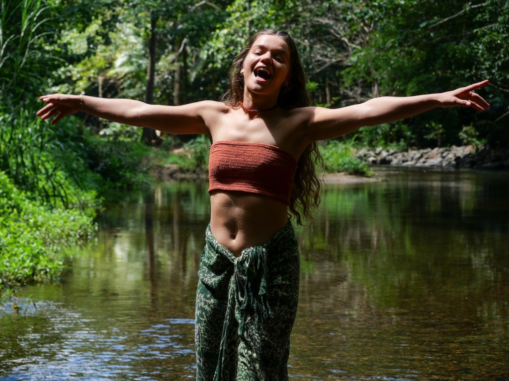Woman standing in water with arms open, embracing nature in a forest setting