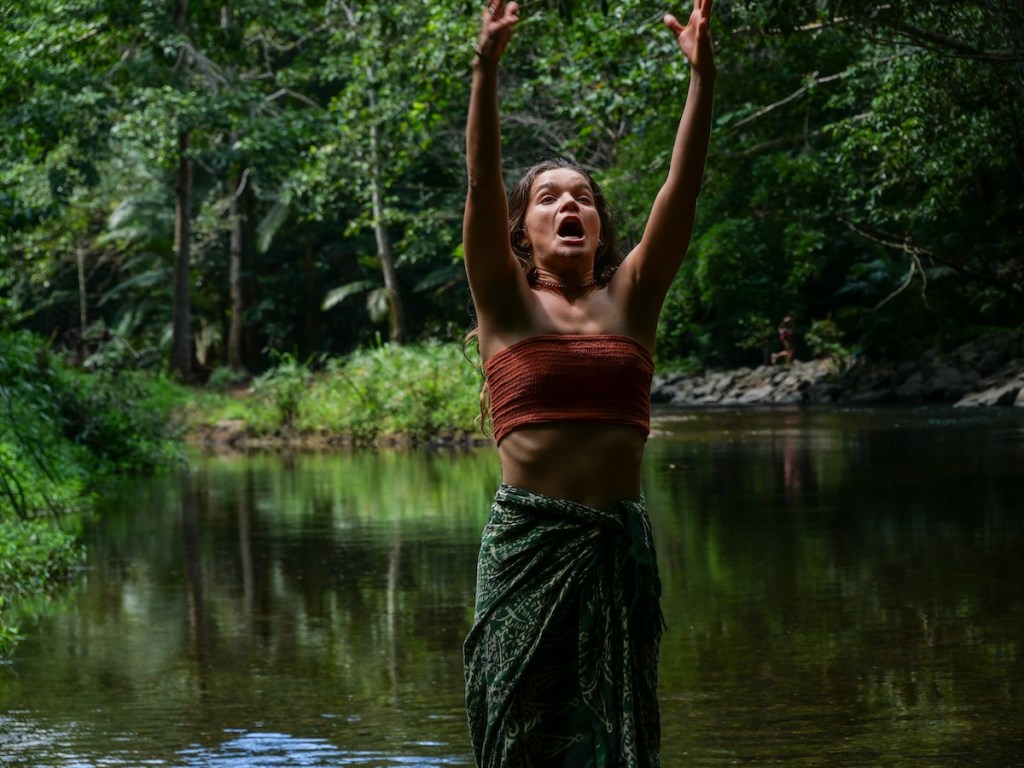 Woman in forest with arms extended, expressing intense emotion