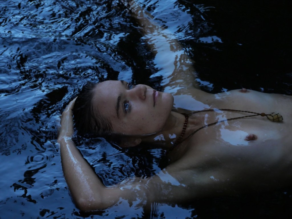 Woman floating in water, partially submerged, surrounded by dark reflections