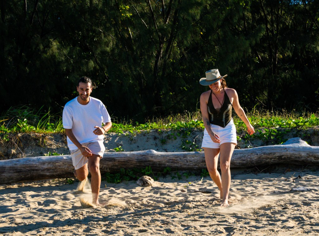 Cristina and Matteo running together on the sand during a couple photoshoot at Yorkeys Knob Beach, Queensland, Australia.